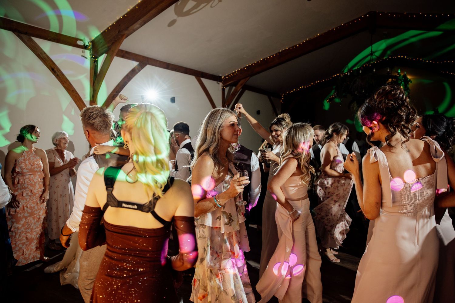 Wedding guests dancing under colorful green lights on crowded barn dance floor.