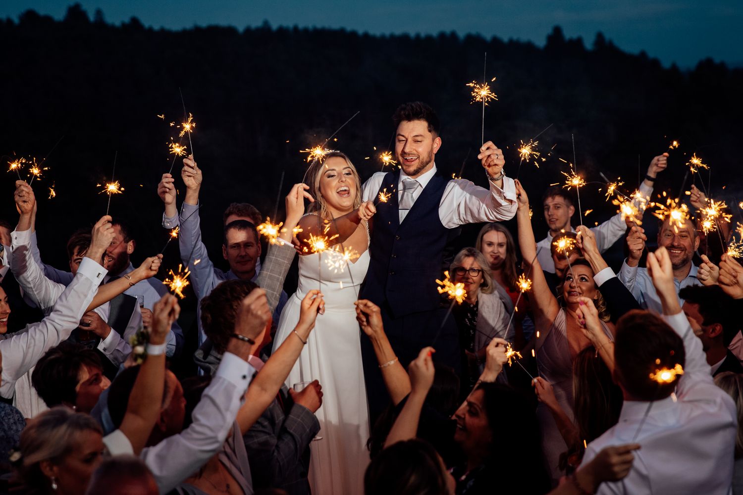 Wedding celebration at night with guests holding sparklers creating a magical atmosphere.