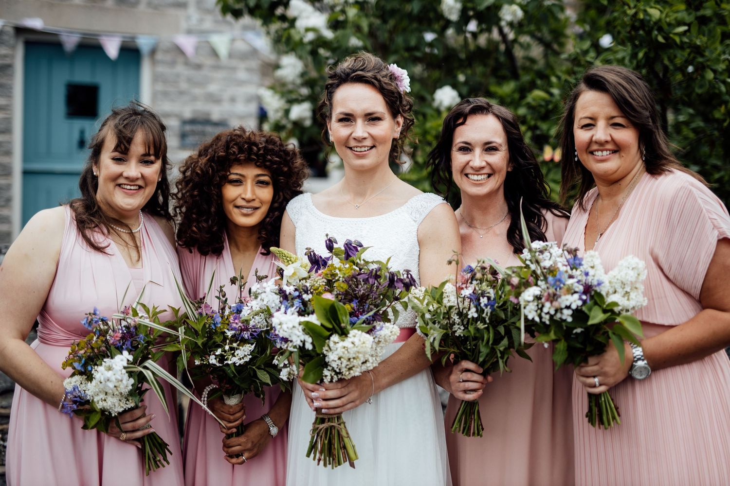 Bridal party in pink dresses holding beautiful wildflower bouquets pose together outdoors.