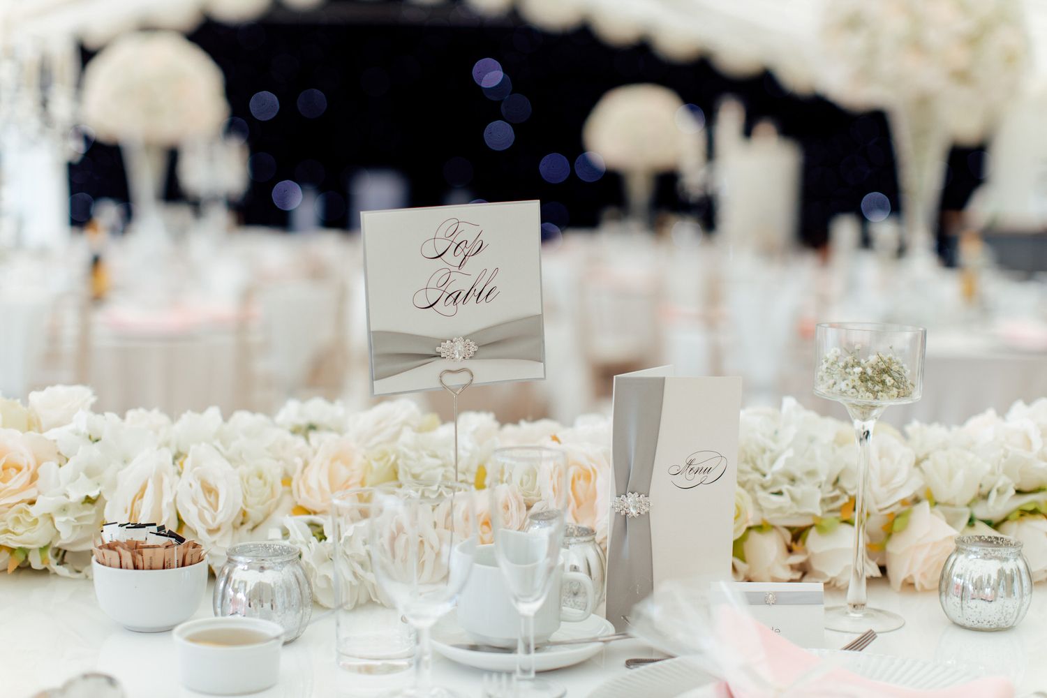 Elegant white wedding reception table settings with floral centerpieces and place cards.