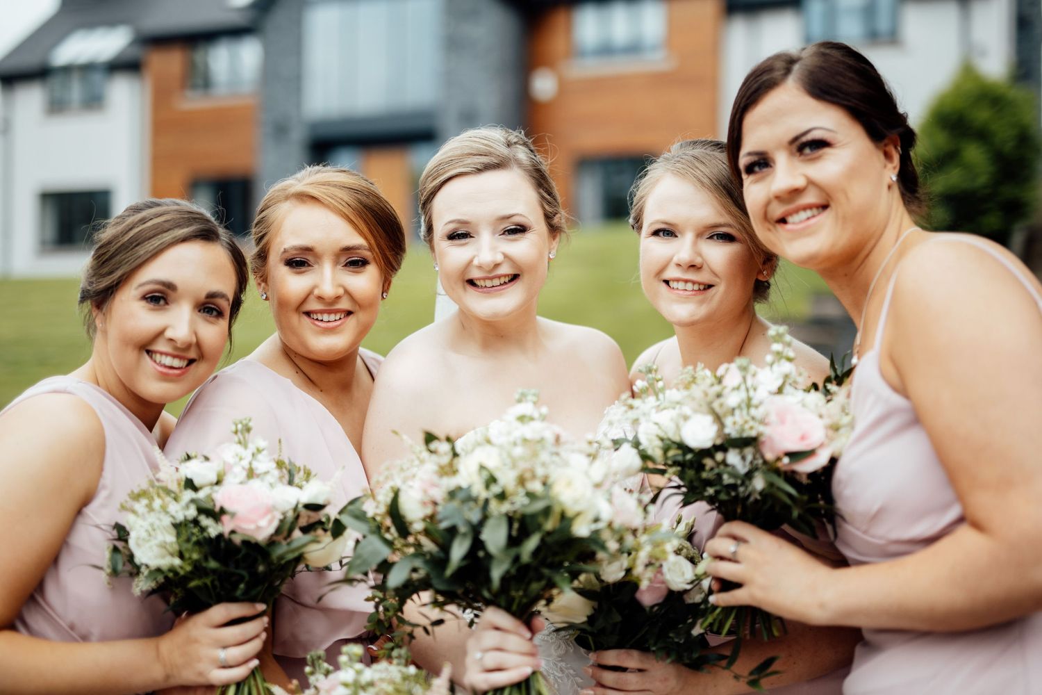 Bridesmaids in pink dresses holding white floral bouquets outdoors.