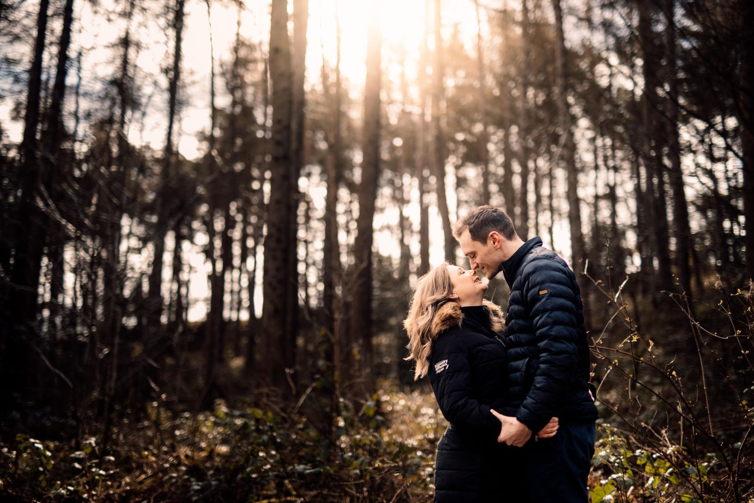 Golden sunset light filters through pine trees as couple shares romantic moment.