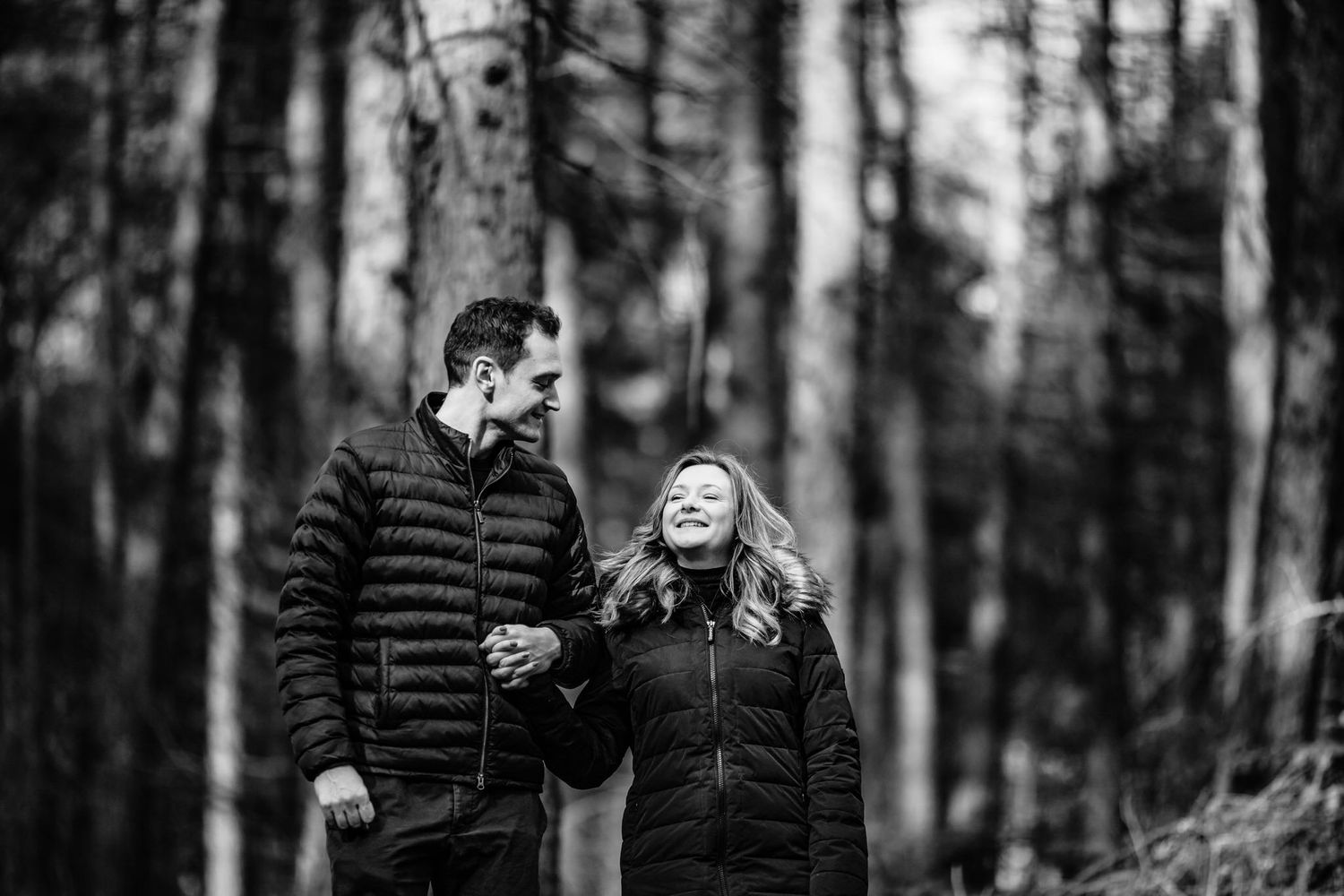 Black and white photo of a couple sharing tender moments in a wooded setting.
