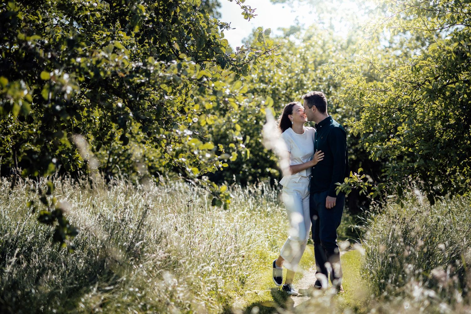 Couple walking through tall grass and wildflowers in natural outdoor setting.