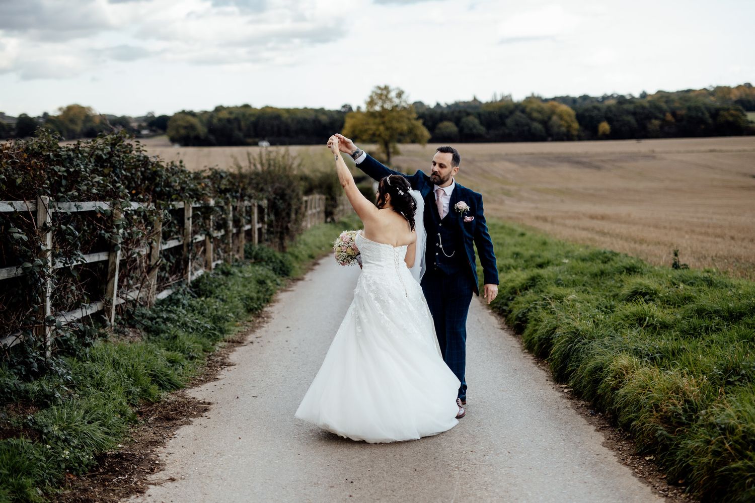 Wedding couple walking along a scenic countryside path surrounded by fields.
