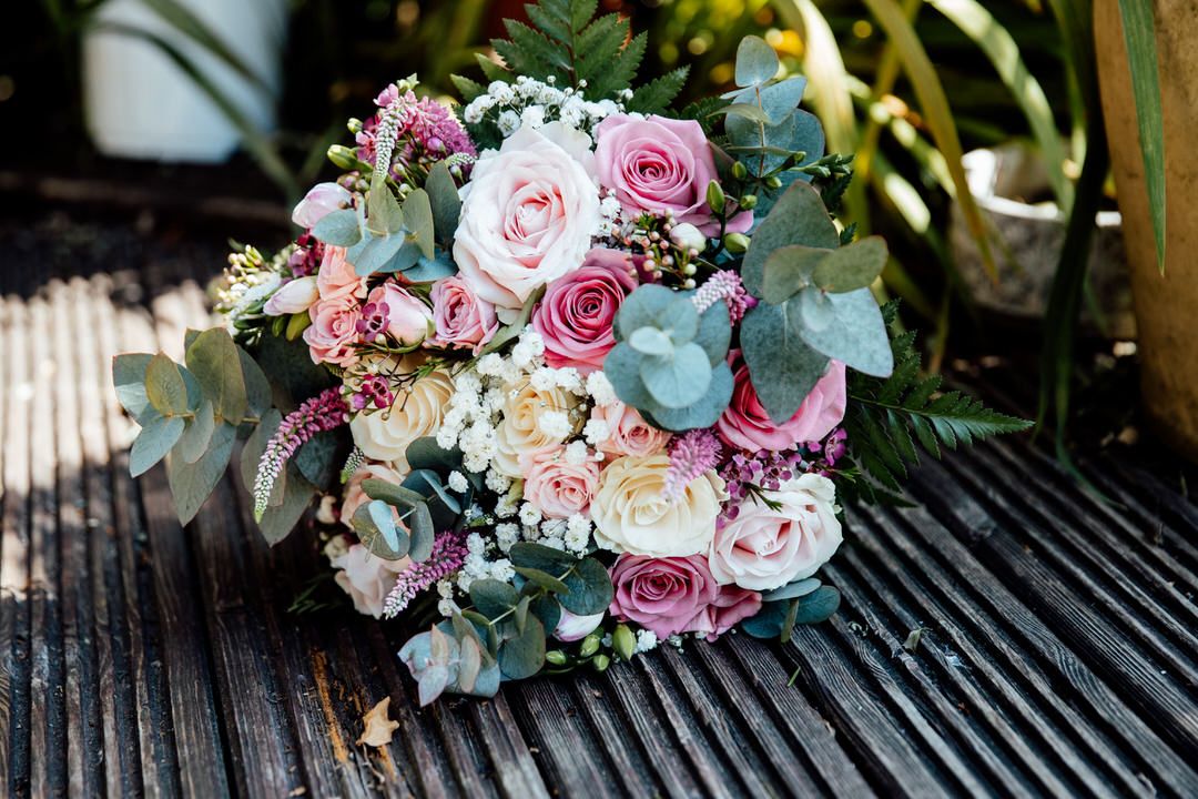 Elegant wedding bouquet with pink roses and eucalyptus resting on dark wooden slats.