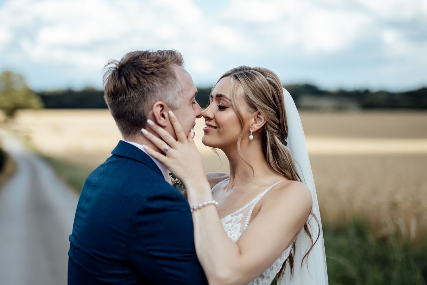 A romantic wedding portrait captured against a backdrop of golden fields and blue sky.