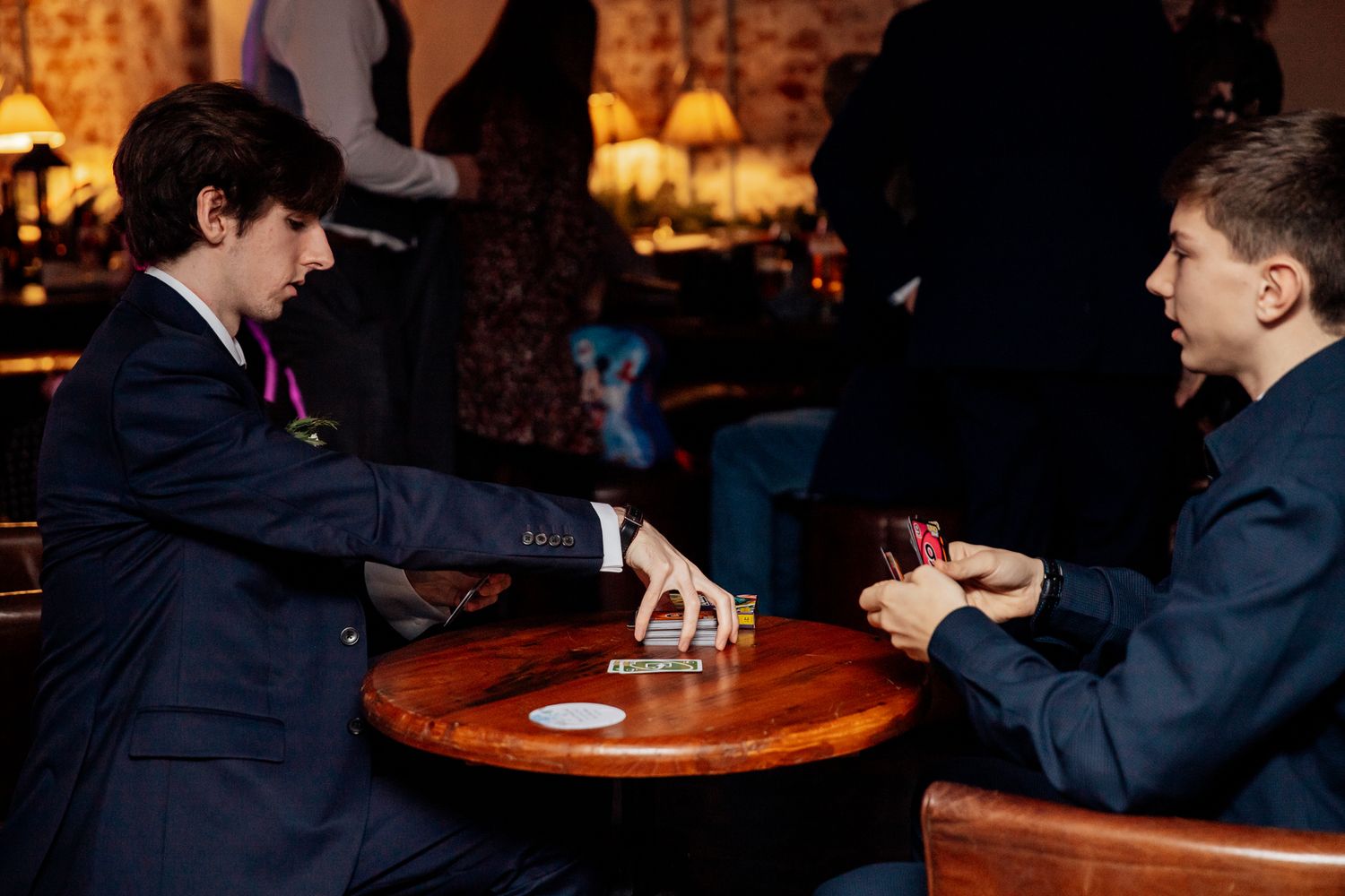 Wedding guests seated at wooden tables in a dimly lit reception venue.