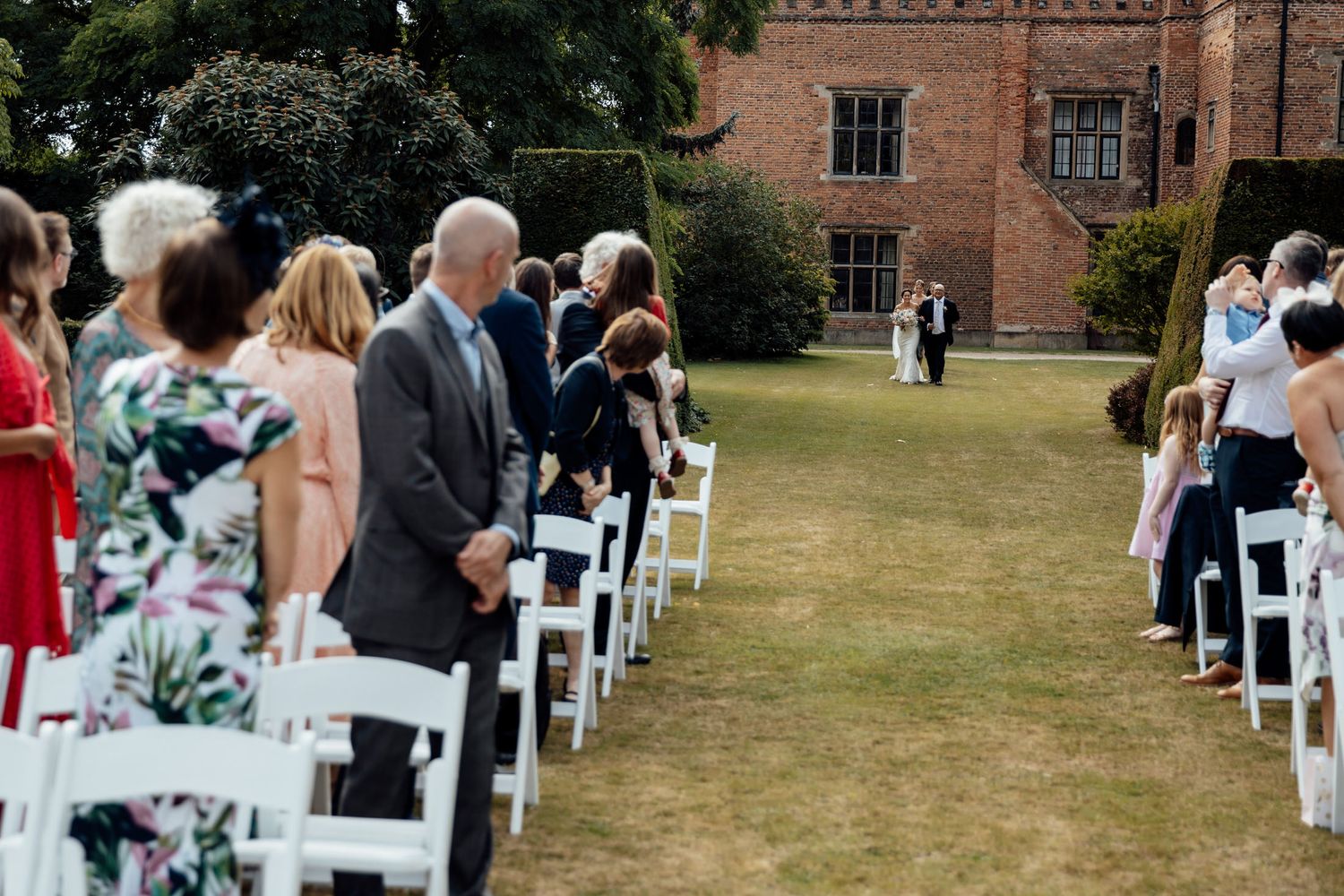Outdoor wedding ceremony setup with white chairs on lawn in front of brick building.