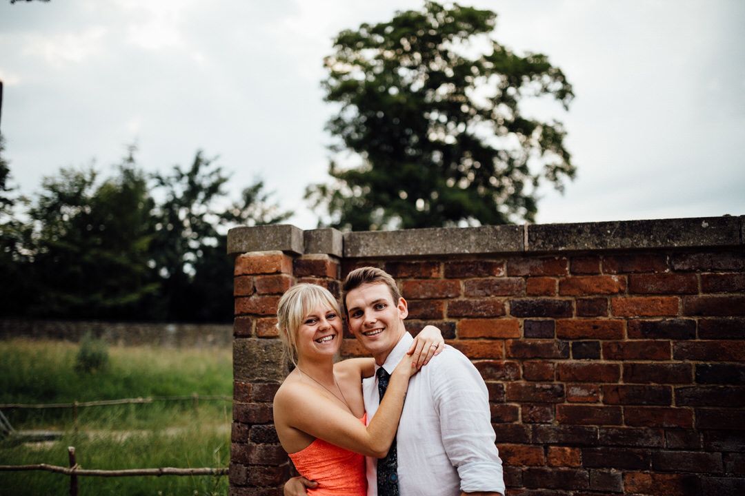 A couple poses intimately against a rustic brick wall in a garden setting.