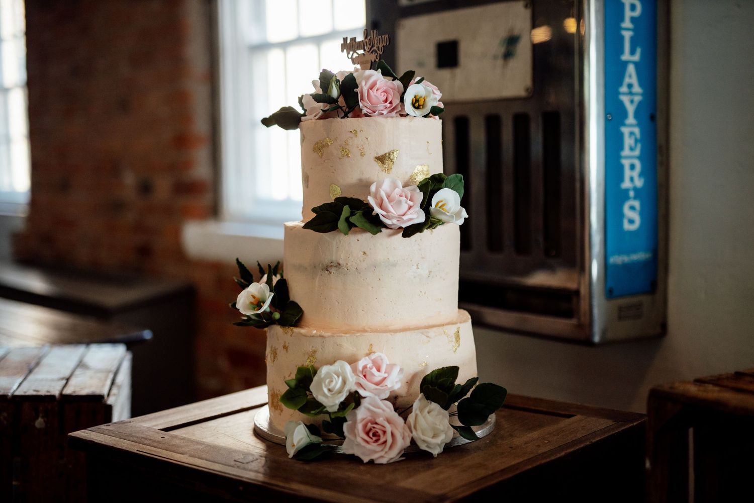 Elegant white wedding cake decorated with pink roses on a wooden table.