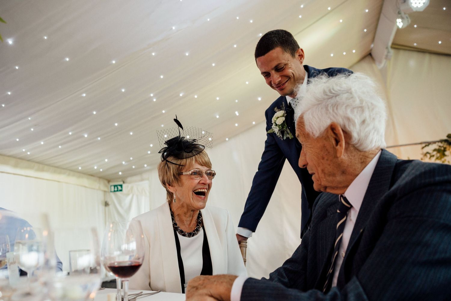 Wedding reception guests enjoying conversation under twinkling ceiling lights.