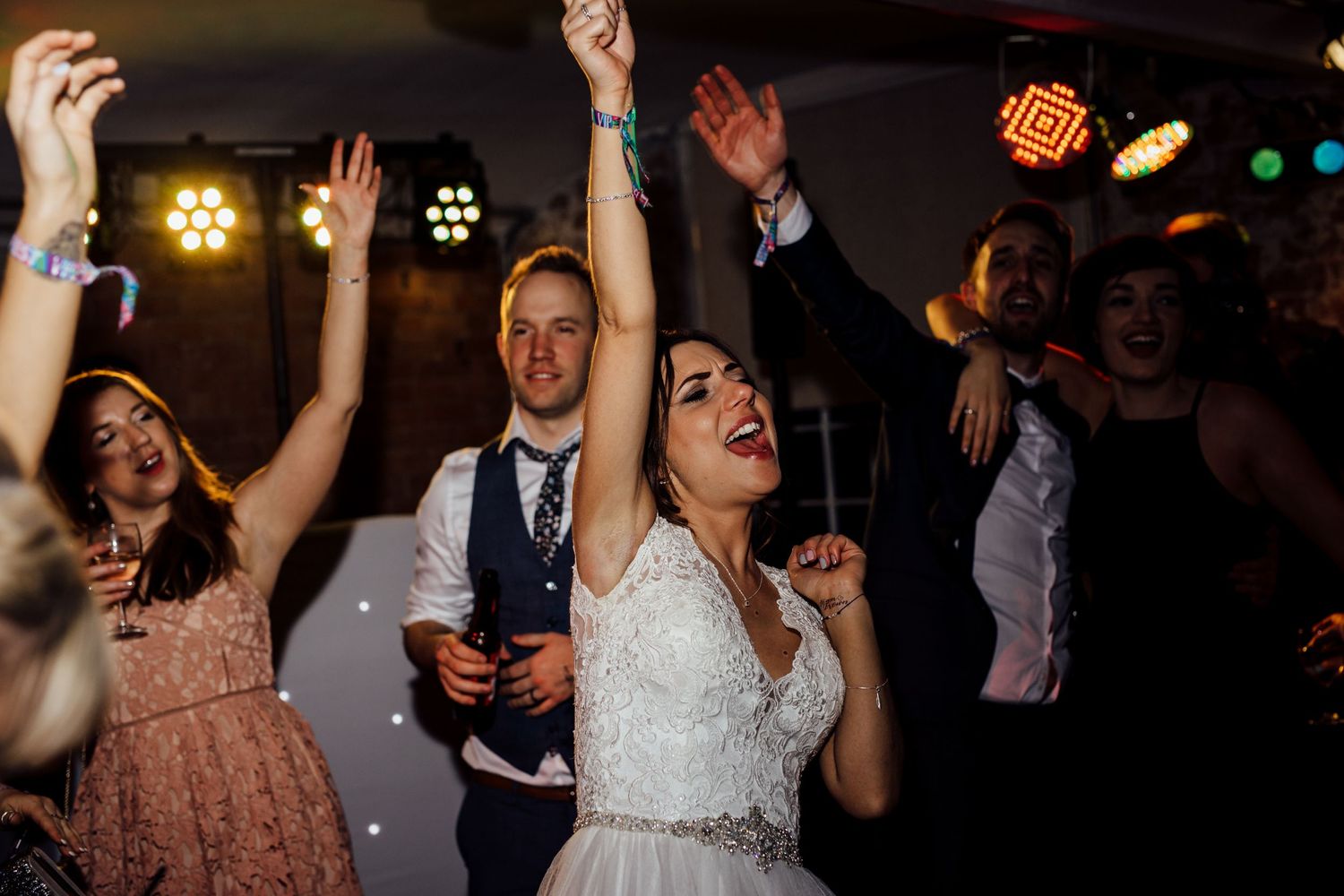 Wedding guests raising their arms and dancing during lively reception party.