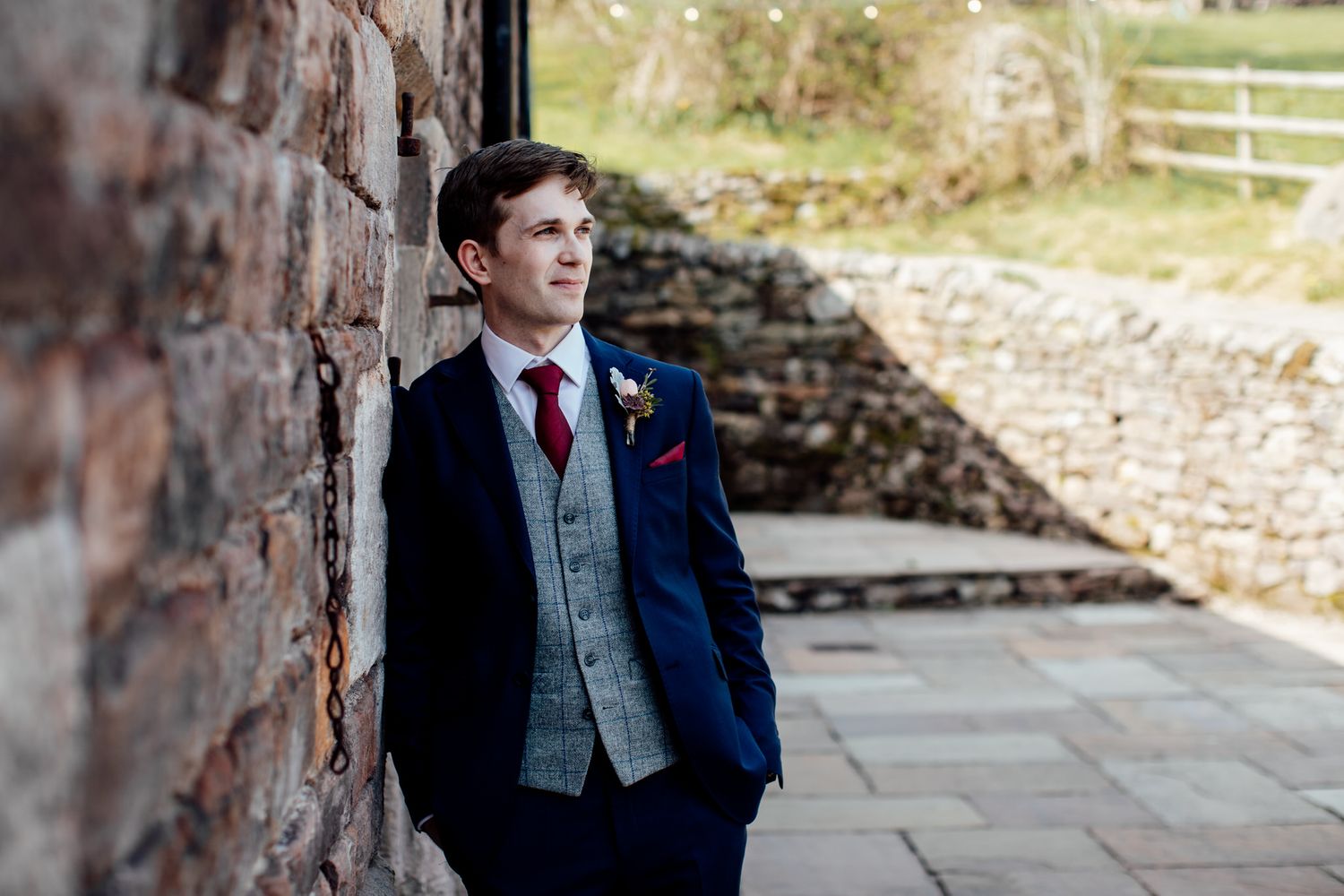 A formal wedding party poses outdoors in navy blue suits and pink dresses against a rustic stone backdrop.