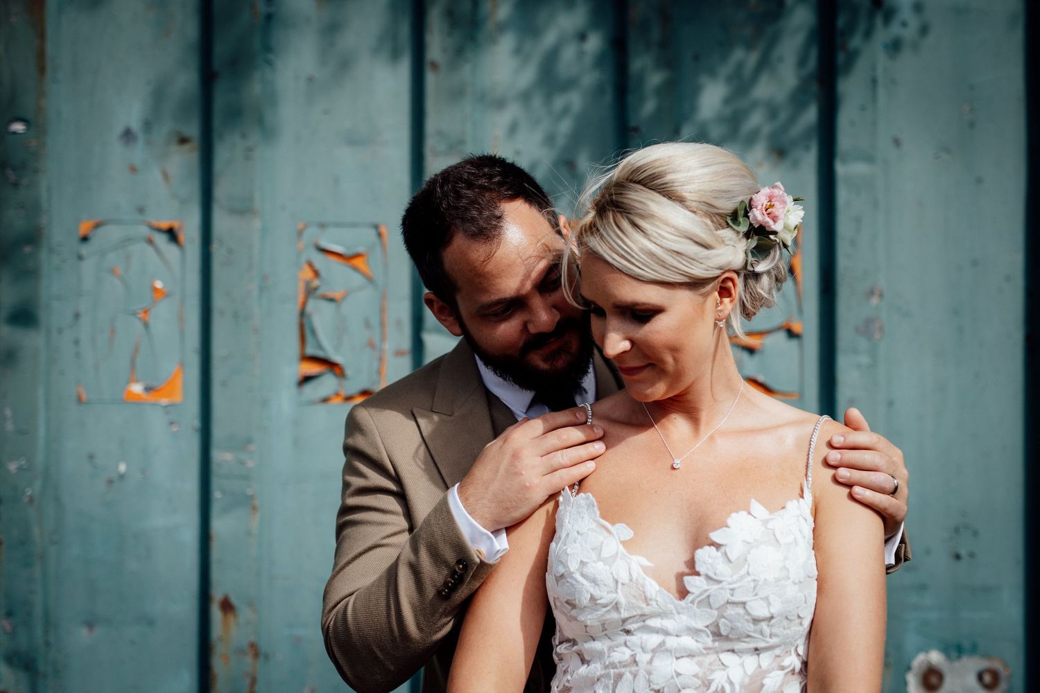 A romantic wedding couple poses against a rustic turquoise wall during their special day.