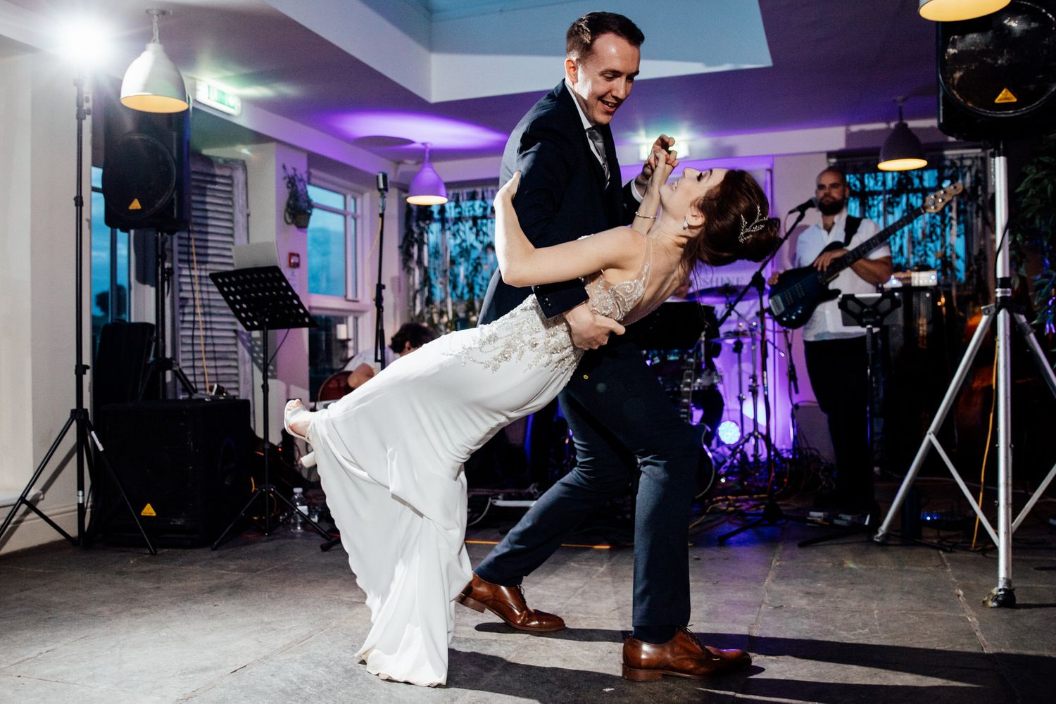 Dramatic dip during first dance at wedding reception with purple lighting and band setup.