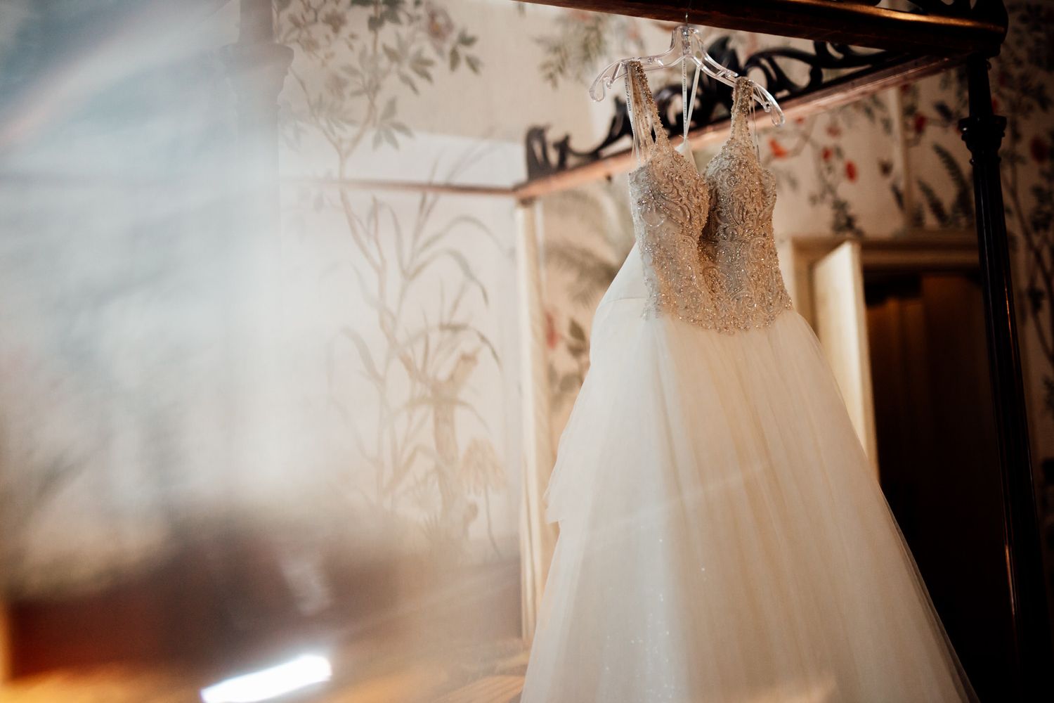 White wedding dress details captured in soft natural light against vintage wallpaper.