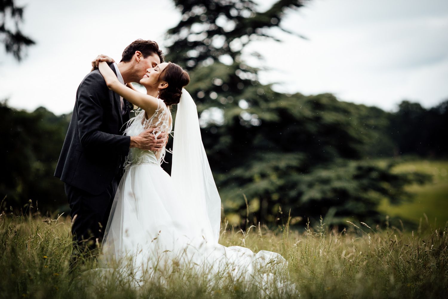 Romantic wedding portrait in tall grass field with overcast sky.