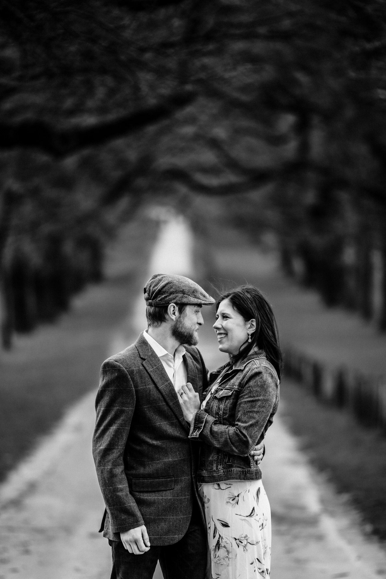 Romantic couple sharing an intimate moment on a tree-lined path in black and white.