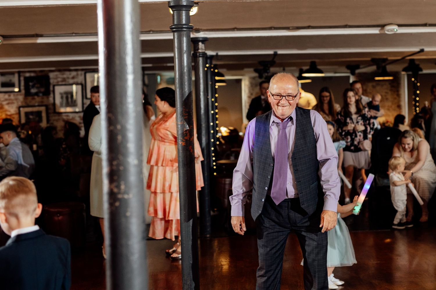 Wedding reception in an industrial venue with exposed pillars and dancing guests.