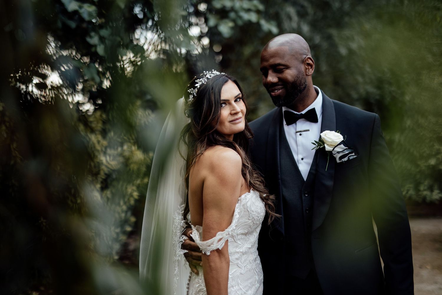 A romantic wedding portrait of newlyweds framed by soft focus foliage.