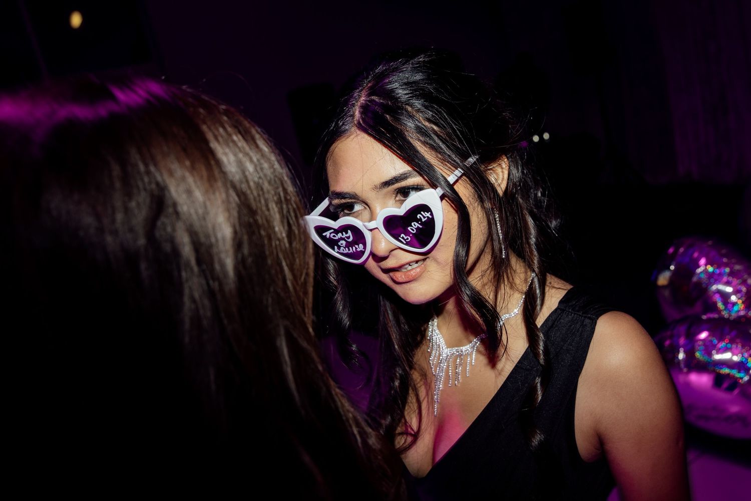 Wedding guests dancing and celebrating with fun party accessories under purple lights.