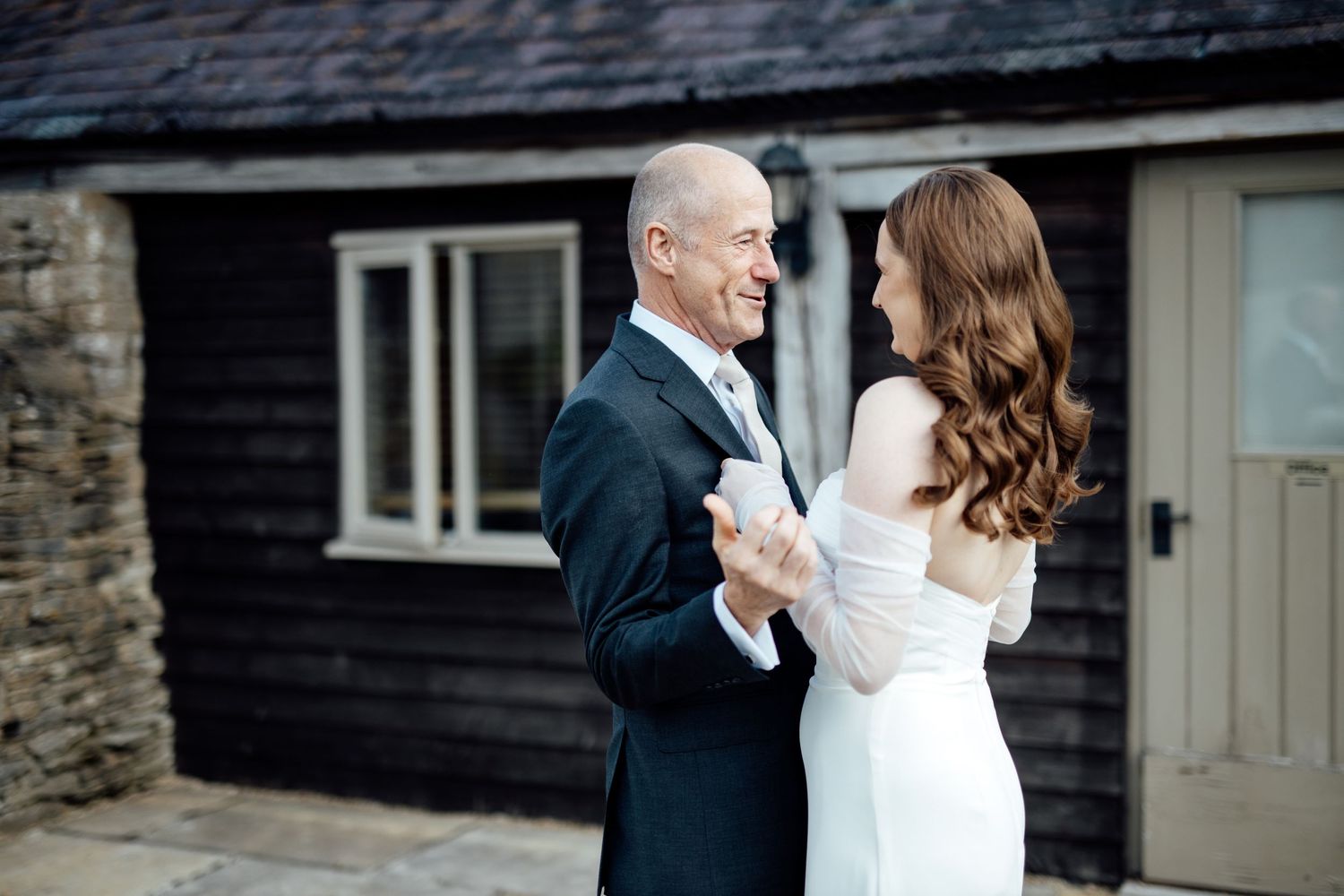 A couple shares an intimate first look moment outside a stone building.