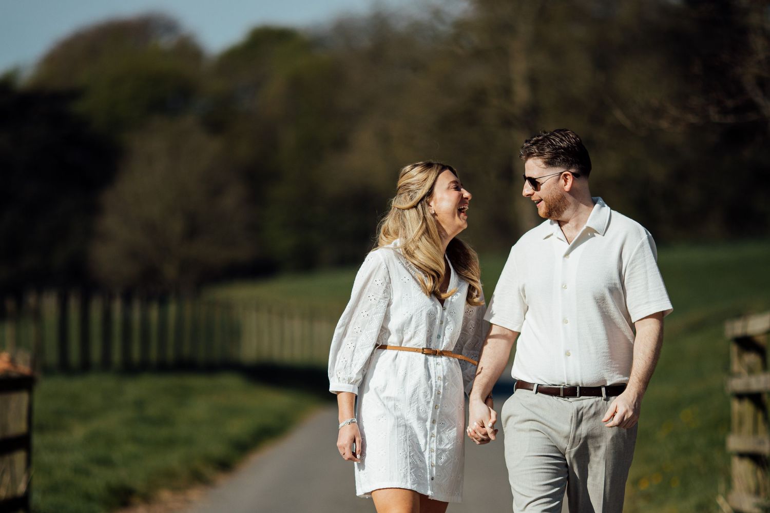 A couple in coordinated white outfits walks together on a sunny spring day.