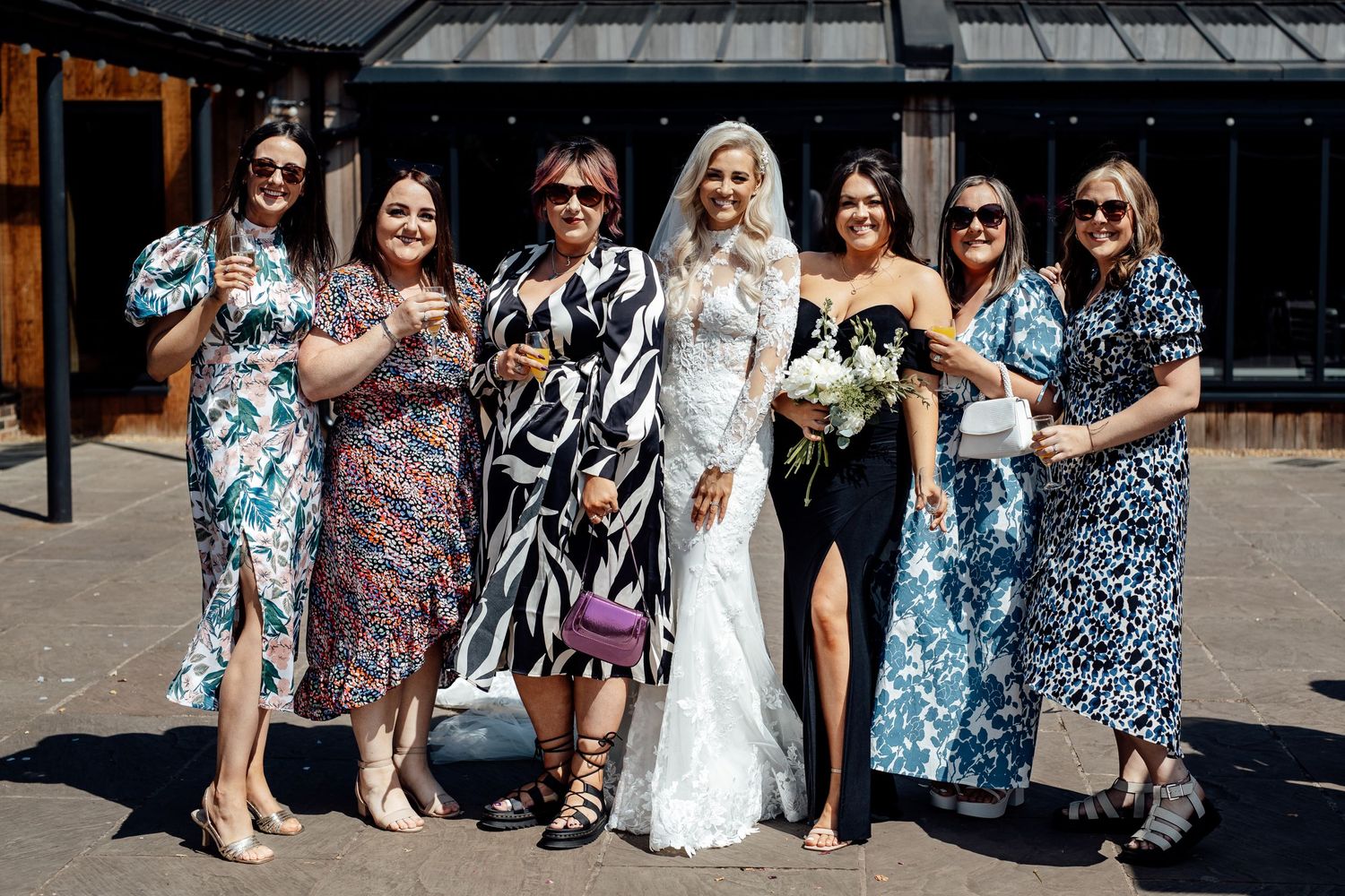 Wedding party poses together outdoors wearing colorful floral prints and summer attire.