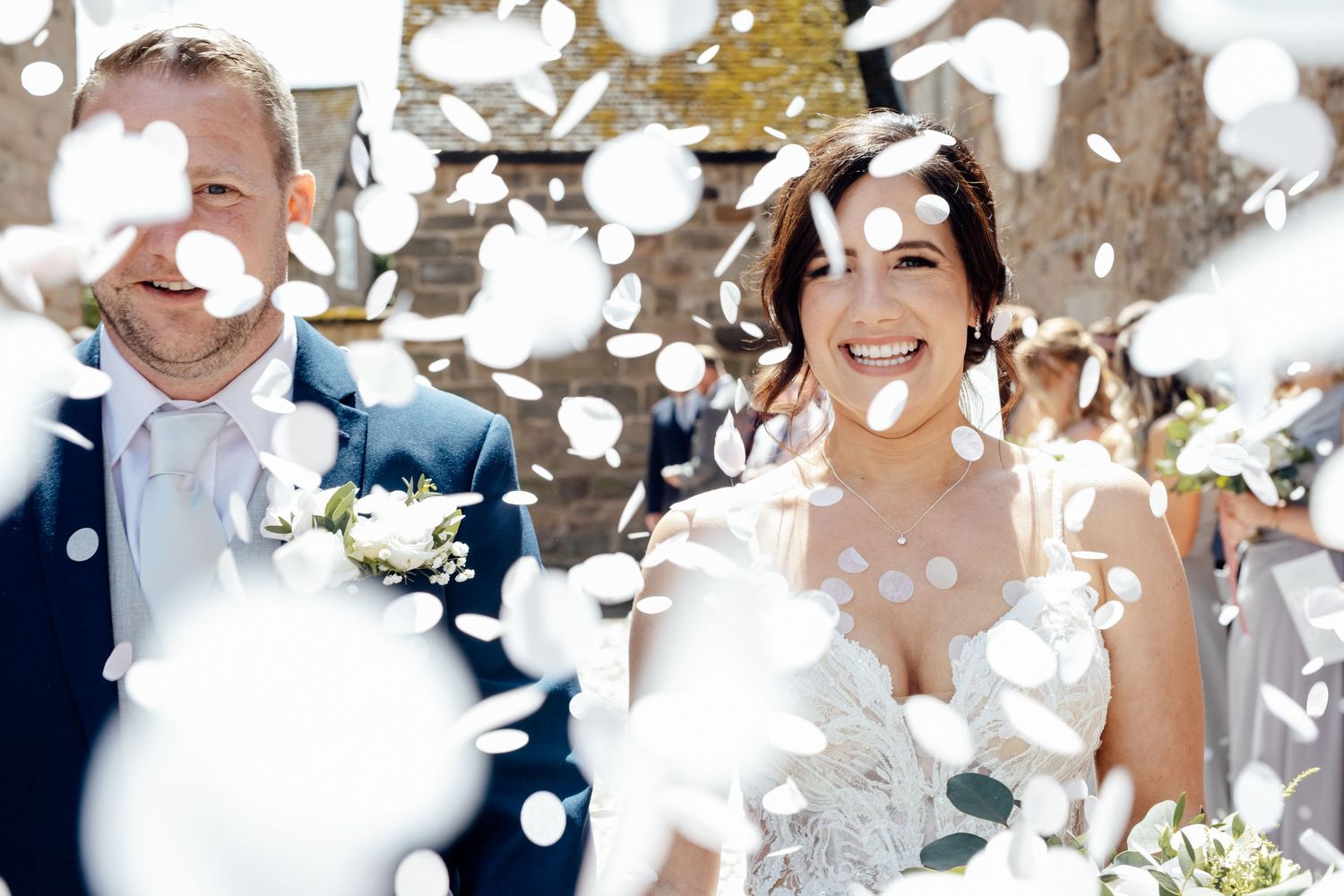 Wedding party celebrates with bubbles floating through the air on a sunny day.