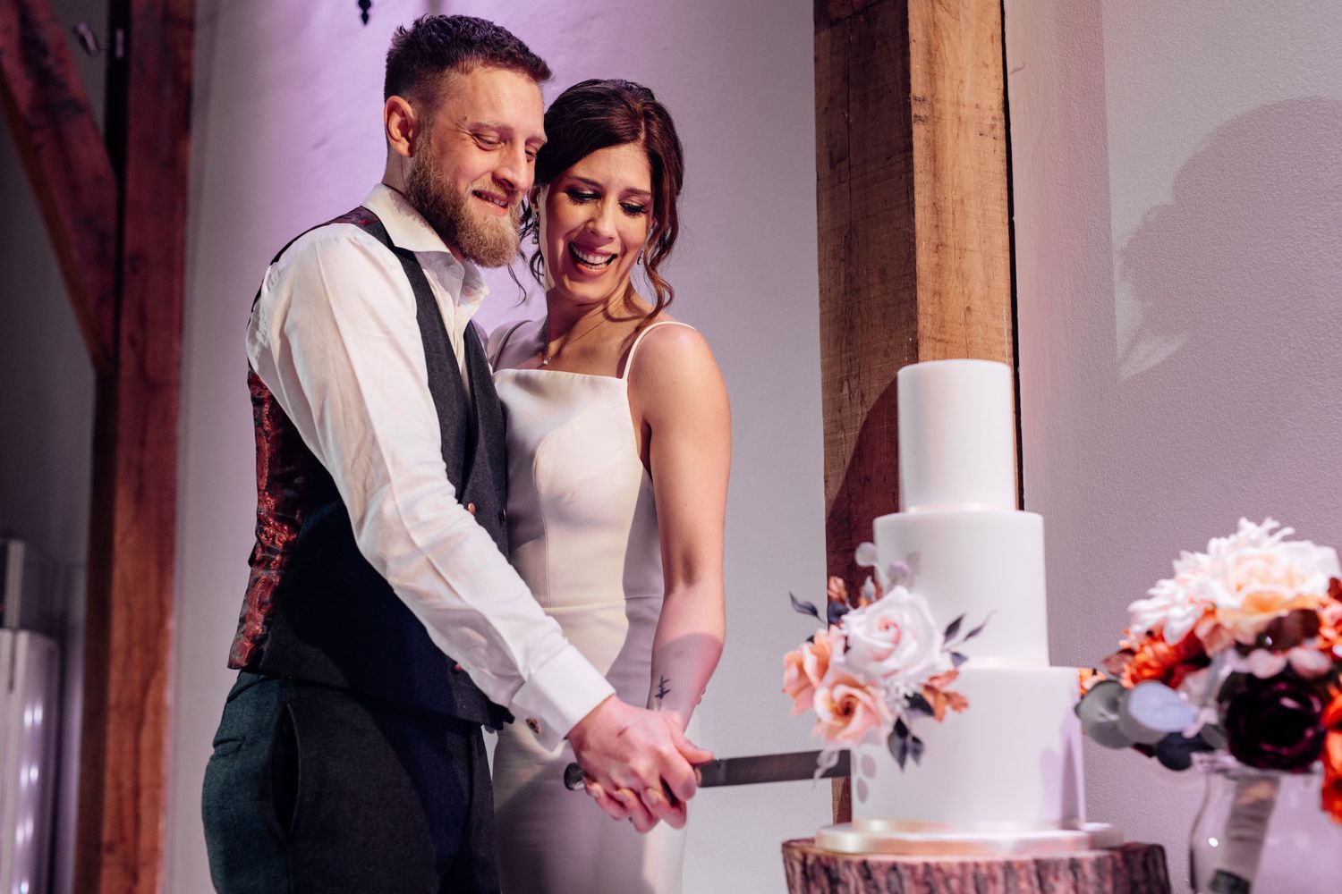 Newlyweds cutting their elegant white wedding cake decorated with pink flowers.