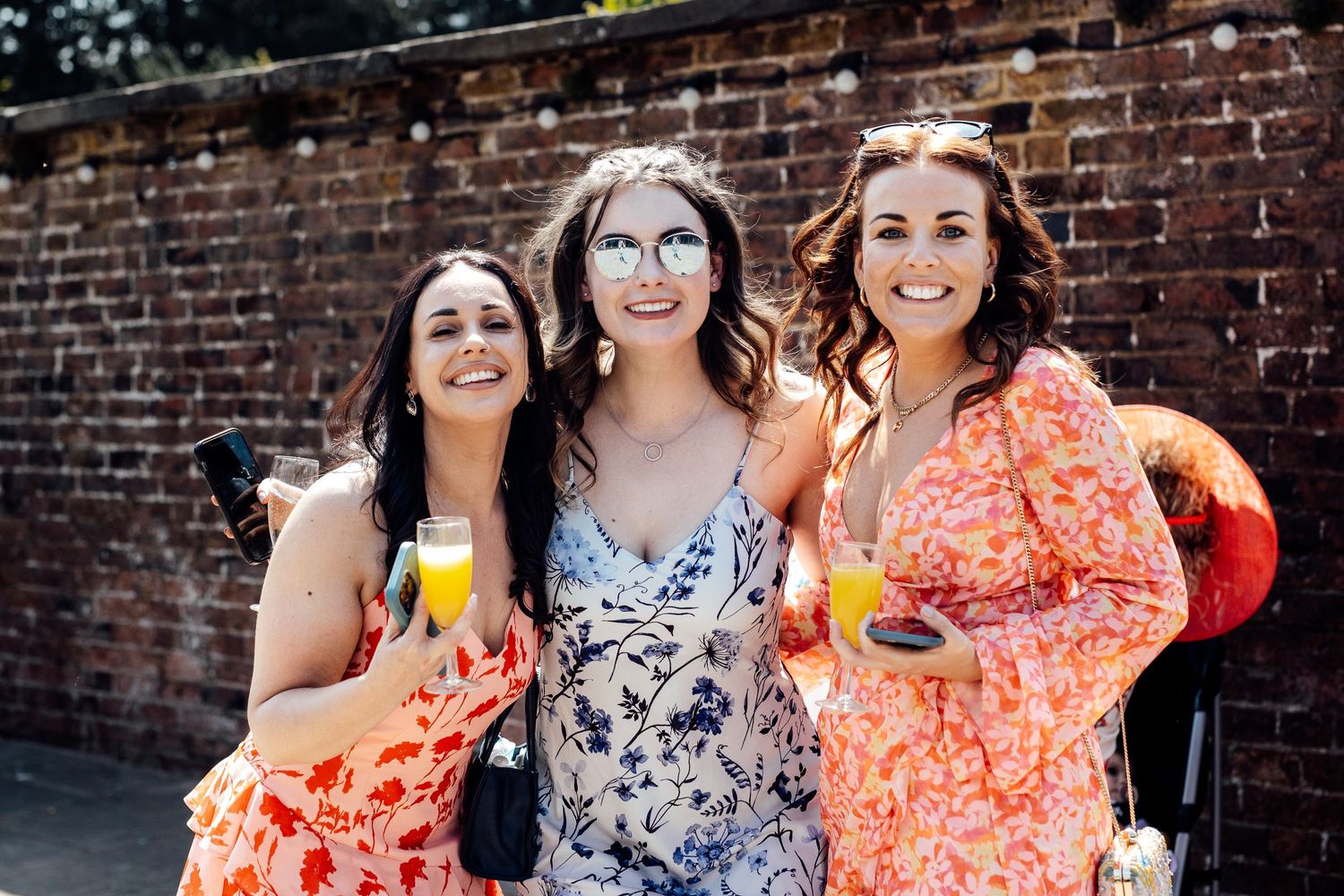 Wedding party members gather for casual photos against brick wall backdrop.