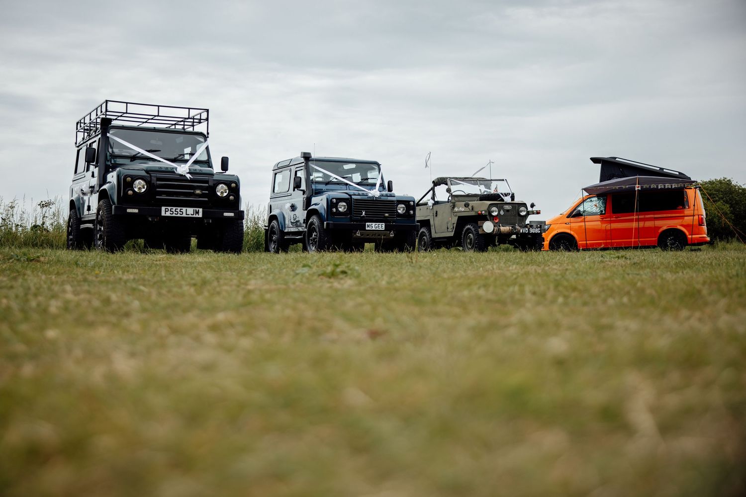 Line of vintage Land Rovers parked with orange vehicle at the end.