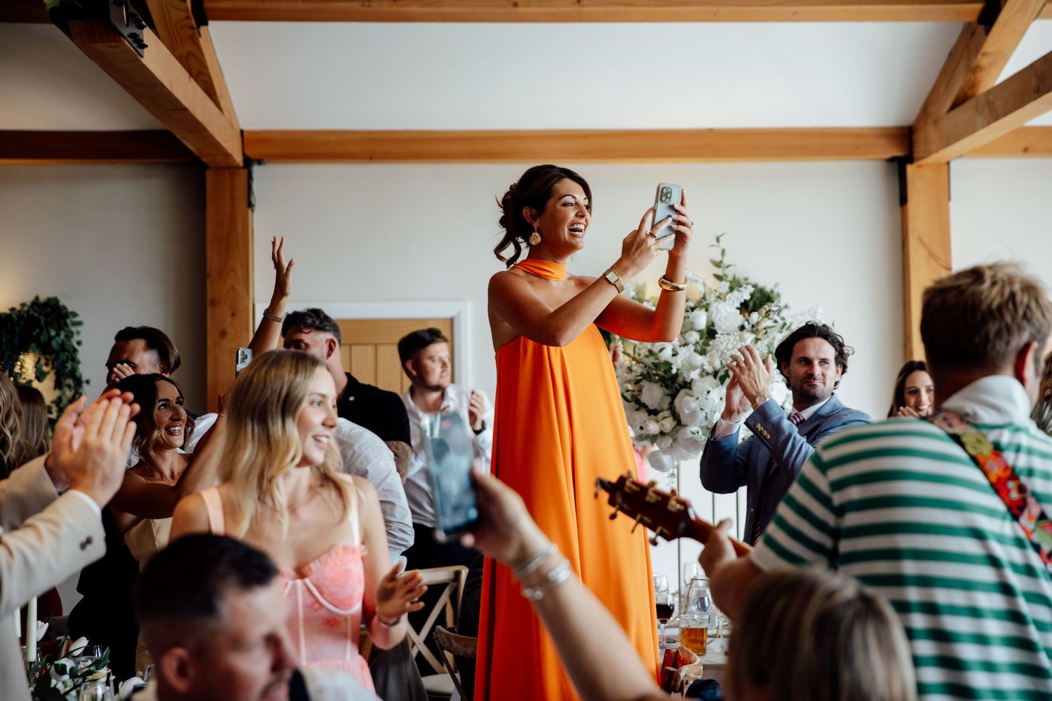 Wedding reception guests dancing and celebrating in a rustic venue with exposed wooden beams.