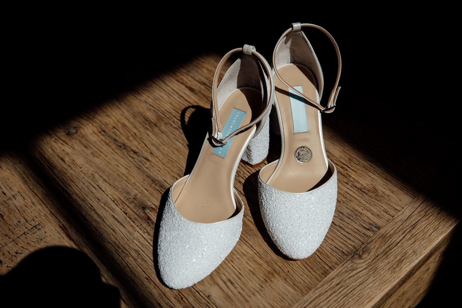Sparkly white bridal shoes on wooden surface with dramatic lighting.