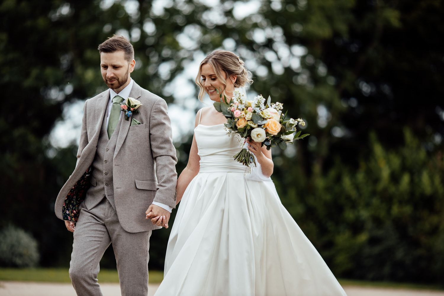 Wedding couple walking together on grass with elegant attire.