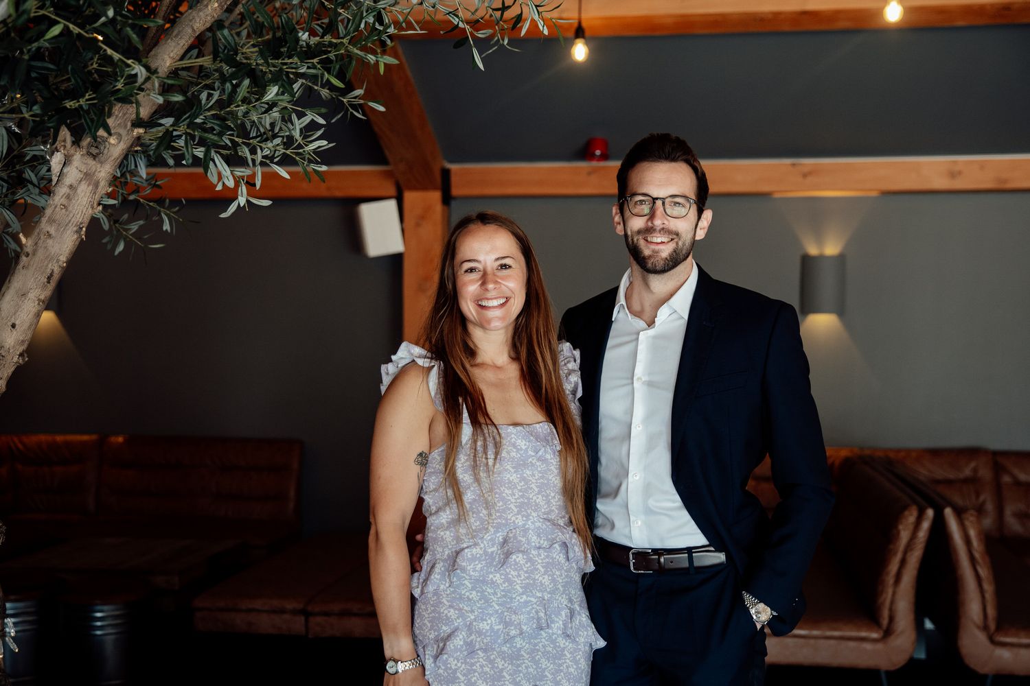 Wedding guests celebrate during an evening reception in a rustic venue with wooden beams.