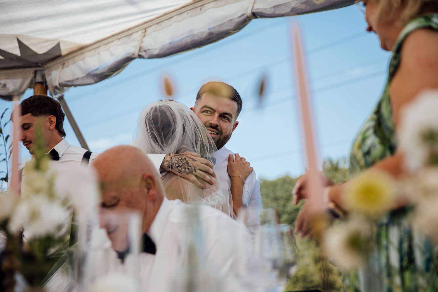 A tender moment captured under a white tent during an outdoor wedding celebration.