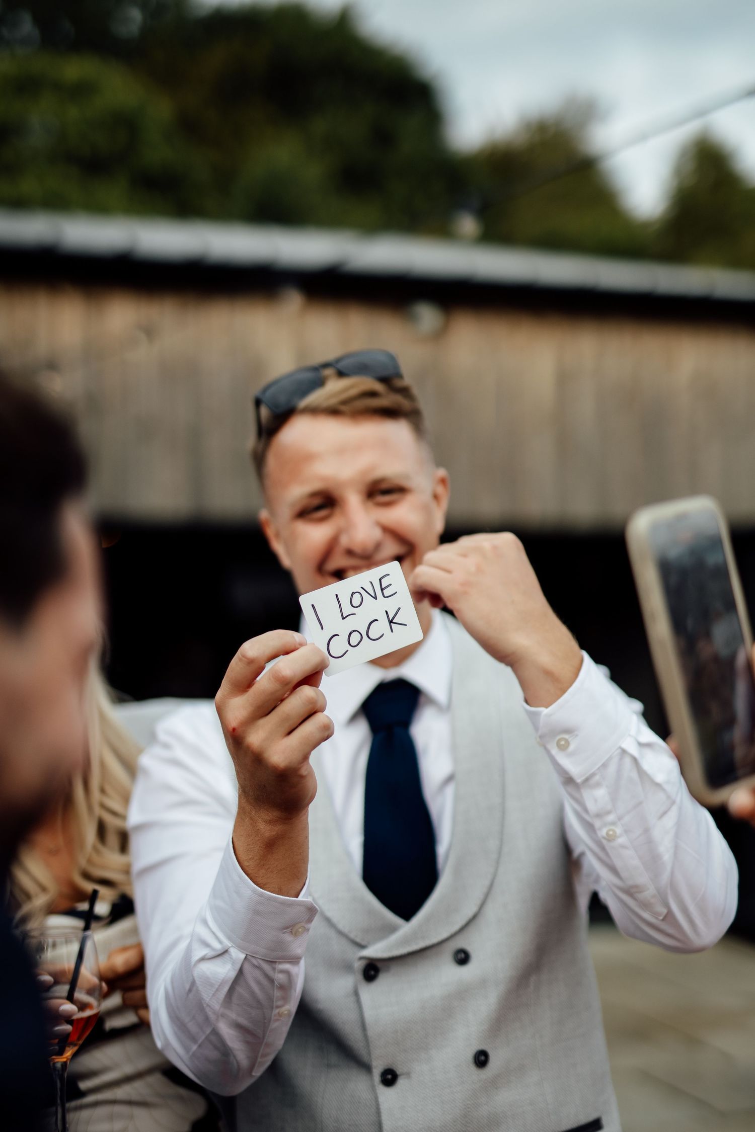 Wedding guest in gray vest holding up small note cards with text.