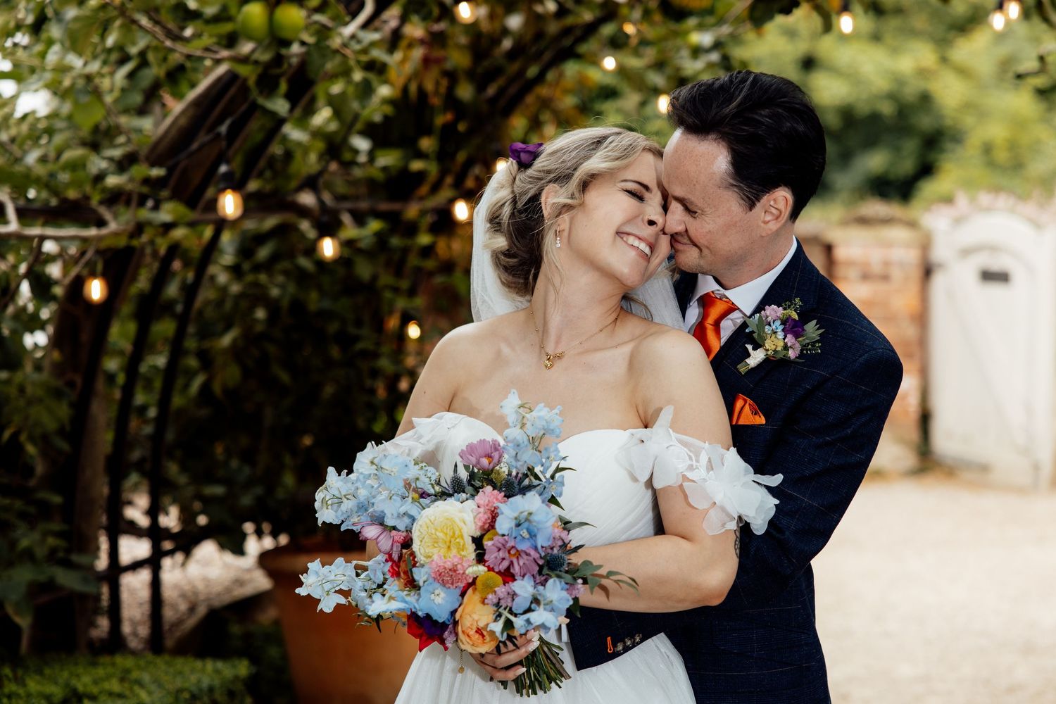 Romantic moment captured in a garden setting with blue and orange floral bouquet.