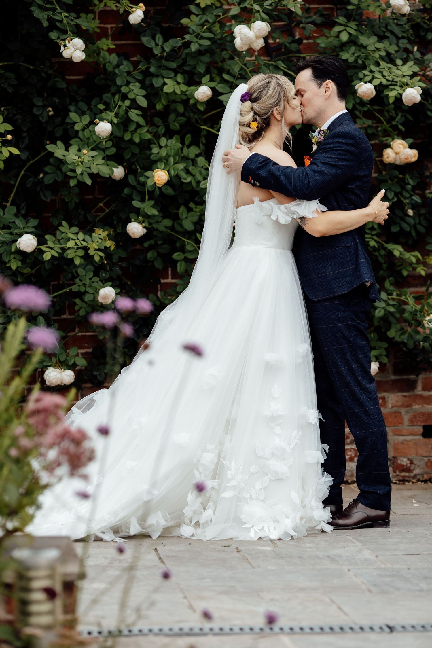 Romantic wedding portrait against a rose-covered wall with the bride's dress flowing beautifully.