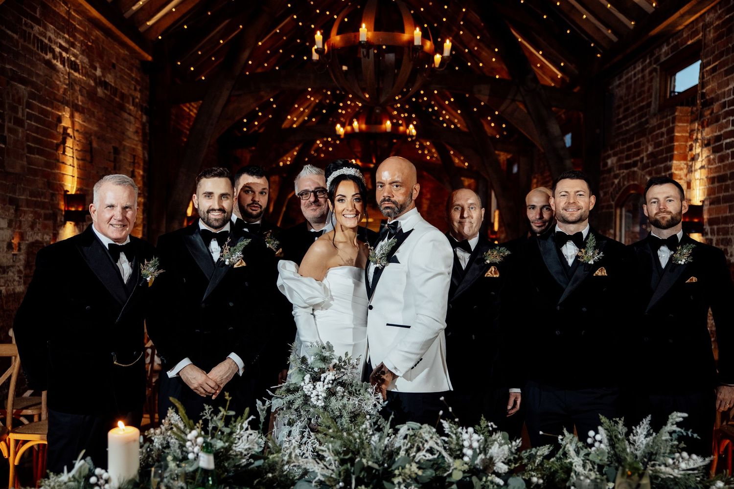 Wedding guests celebrate during an evening reception in a rustic brick venue with warm lighting.