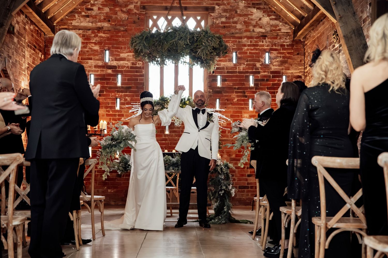 Rustic brick wall wedding venue interior with hanging lights and cross-back chairs.