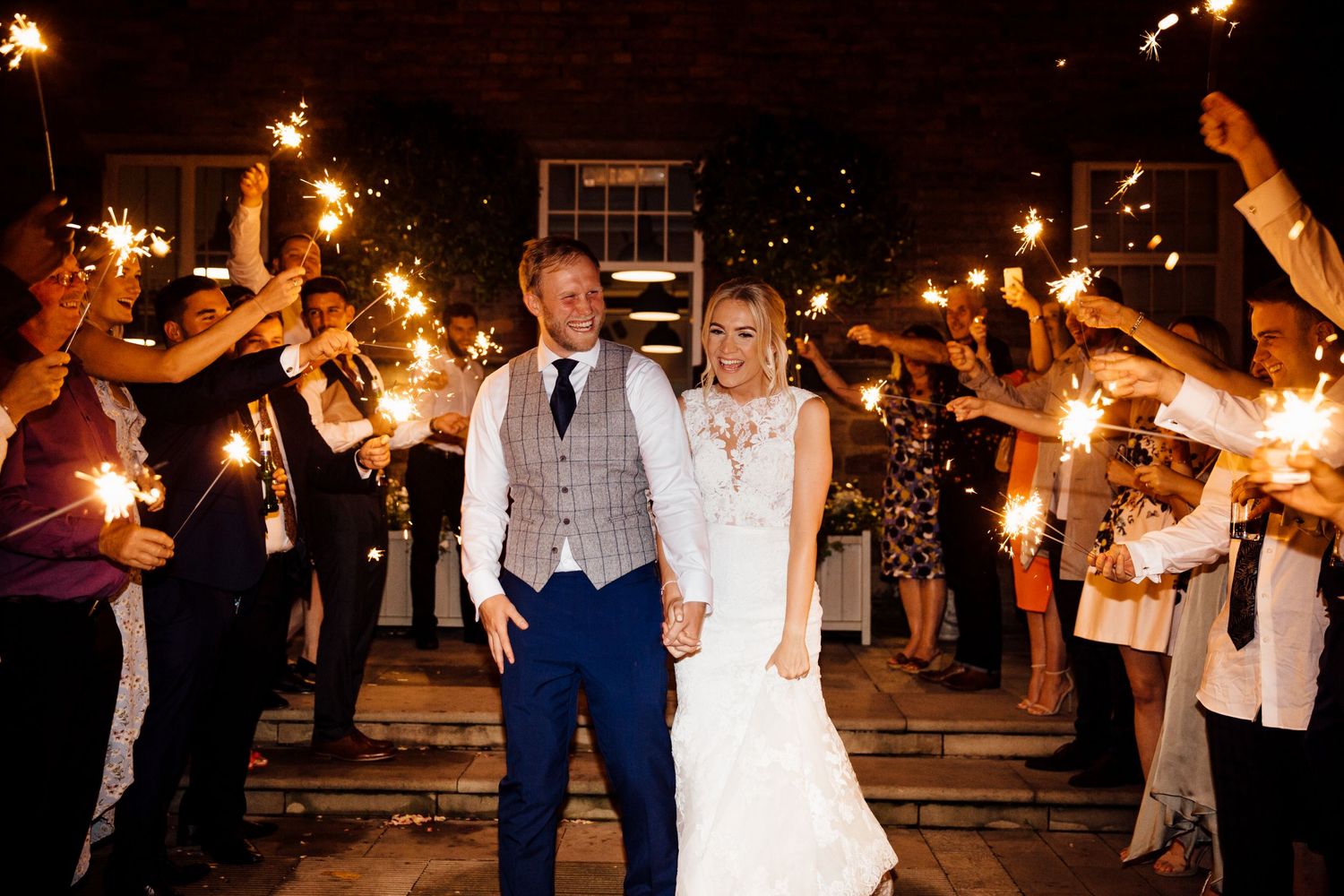 Newlyweds stand together while guests create a sparkler exit tunnel.