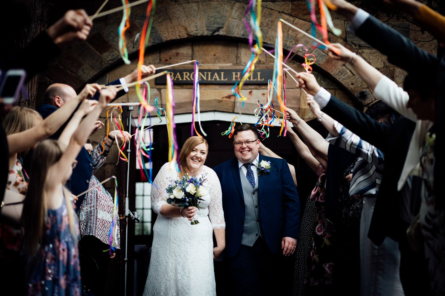 Wedding party forming an archway with colorful ribbons for the newlyweds.