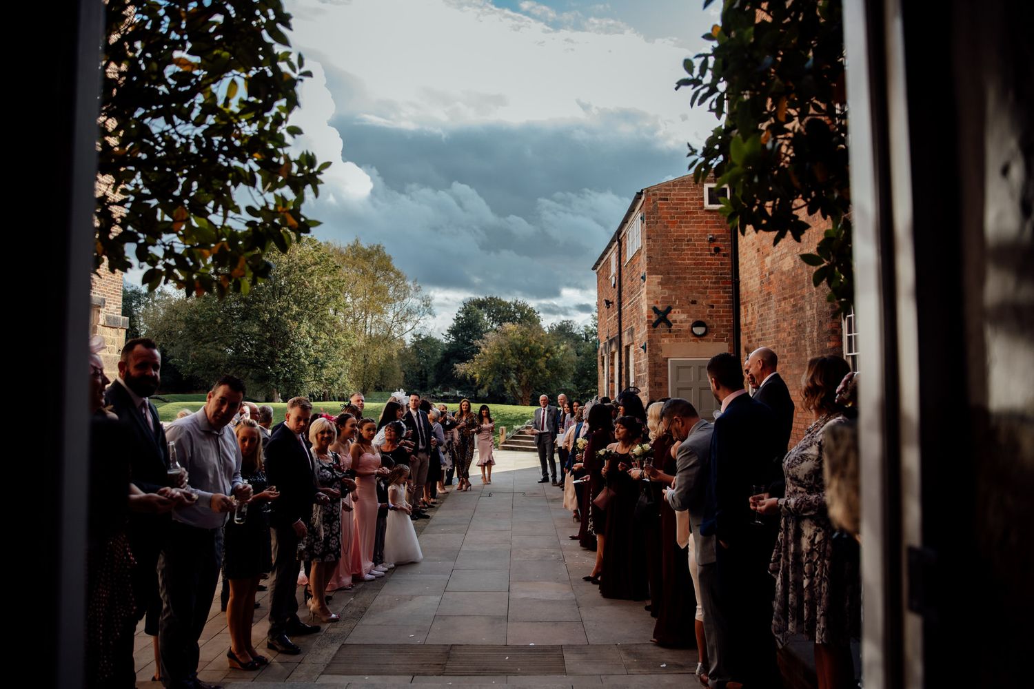 Wedding guests line pathway under blue sky for outdoor ceremony.