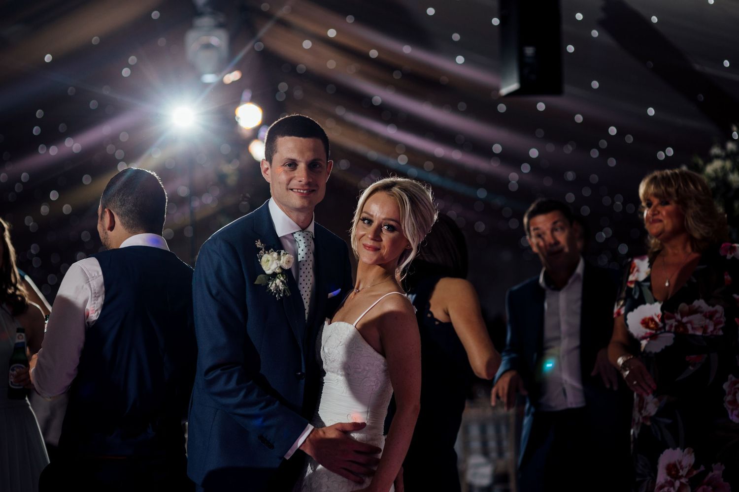 Wedding reception guests mingling and dancing under atmospheric lighting.