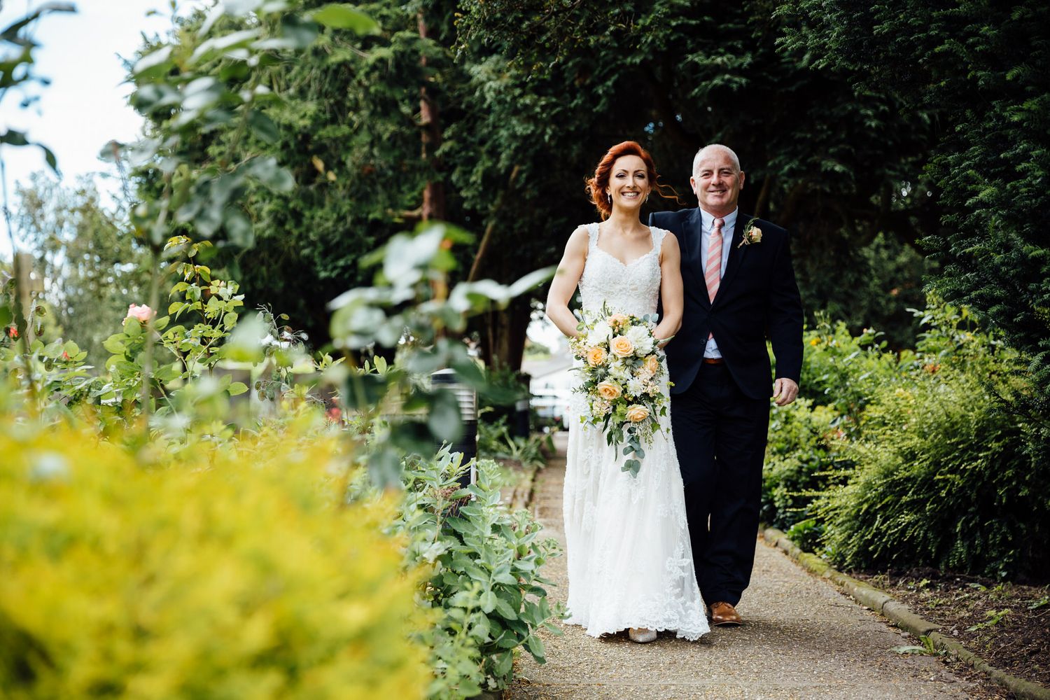Wedding party walking through lush garden path during summer celebration.