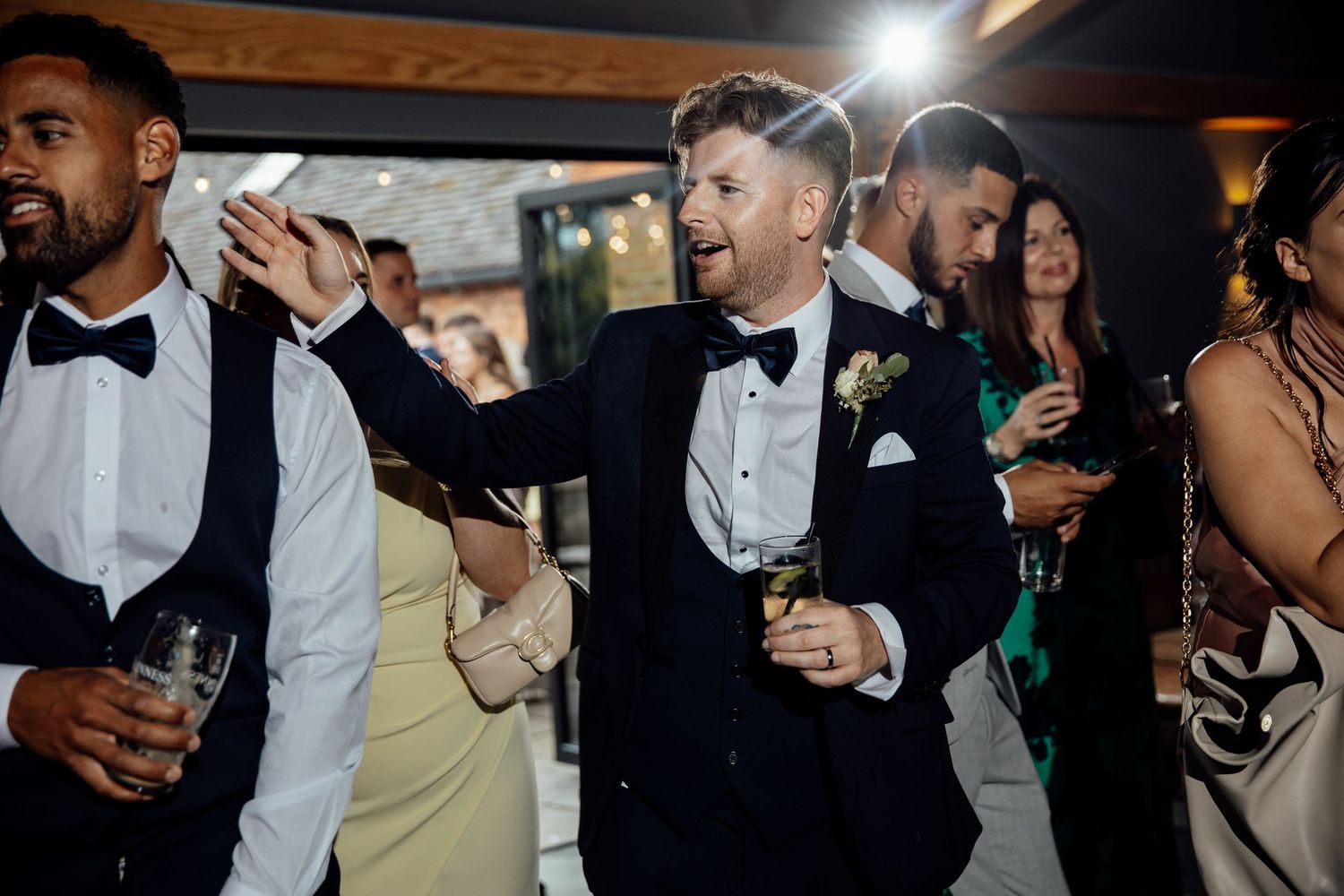Reception guests mingling and celebrating with drinks under wooden beams.