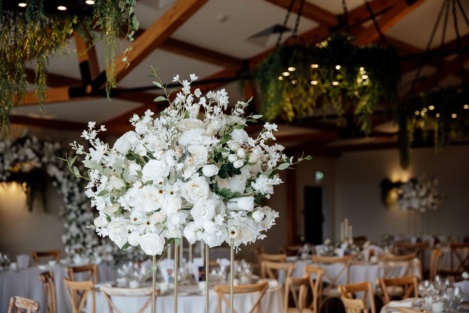 Wedding reception venue decorated with elegant white floral centerpieces and hanging lights.